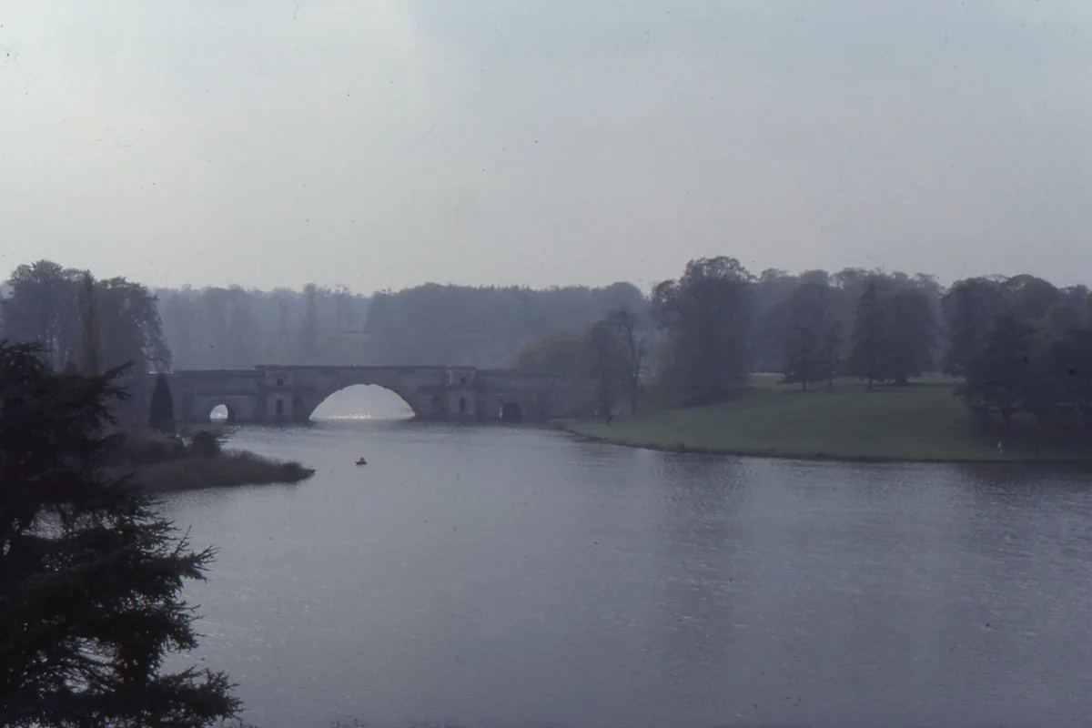 Vanbrugh's Grand Bridge at Blenheim seen across still, misty water, framed by dark trees