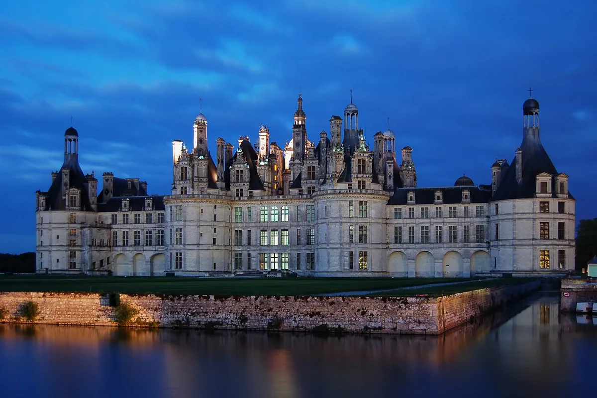 The Château de Chambord lit at night, reflected in the river Cosson