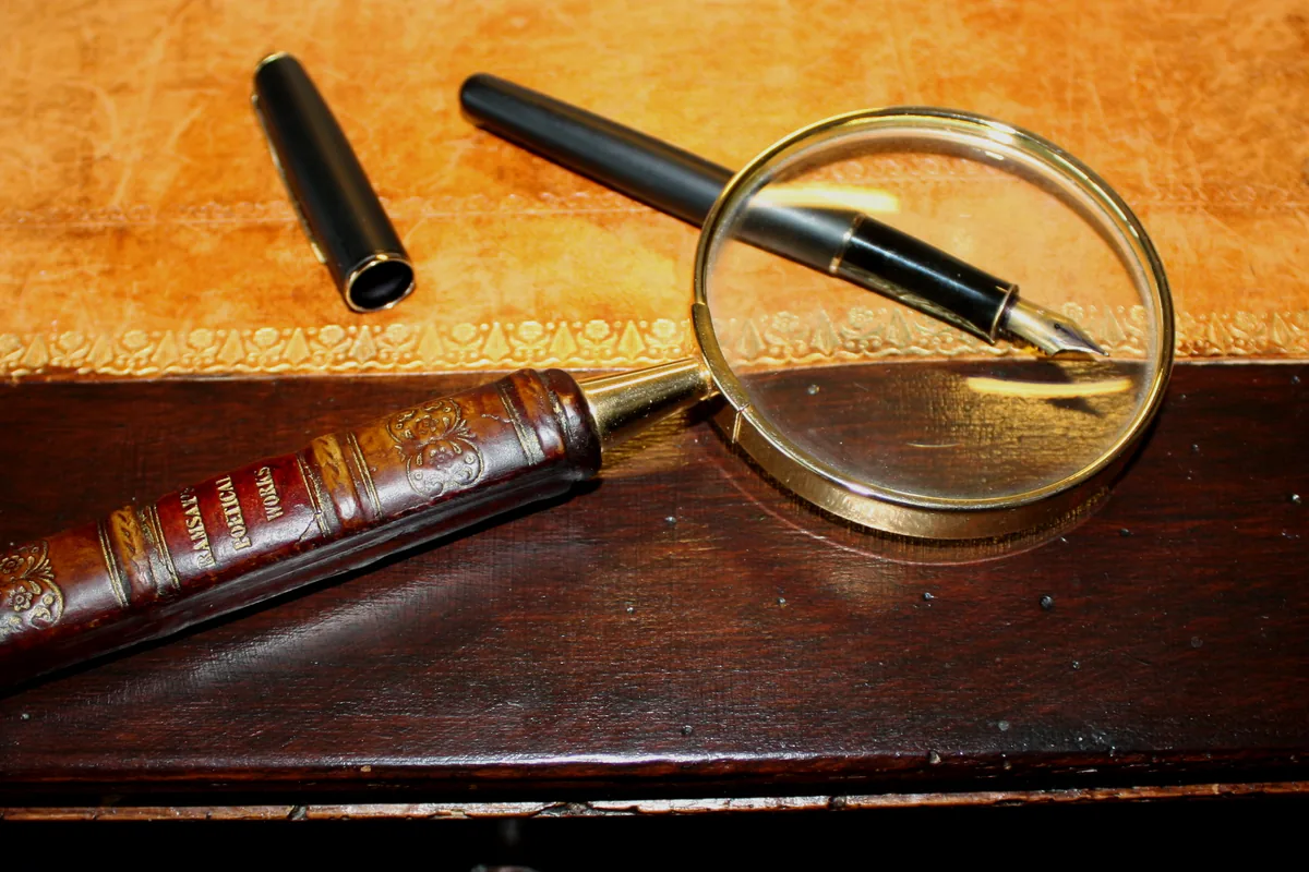A brass magnifying glass and fountain pens on a seventeenth-century table
